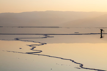 Photographer taking pictures of sunrise on the shore of the Dead Sea