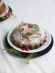 traditional christmas cake decorated with berries, icing sugar and green sprigs on a white table
