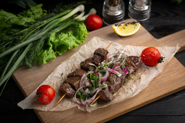 beef skewers with pickled onions and cilantro on a wooden board decorated with leafy greens