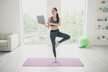 Fototapeta premium Pełnowymiarowe zdjęcie pozytywnej, uroczej, sportowej dziewczyny w pracy, wyszukiwanie przy komputerze, filmy o wykonywaniu ćwiczeń sportowych, uprawiających crossfit, dobre samopoczucie, rozgrzewka, stojąca na fioletowej macie w siłowni w studiu