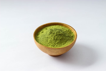 Closed up and top view extract Mathcha green tea powder in mini brown wooden bowl on white paper background.