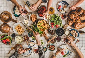 Turkish breakfast. Flat-lay of peoples hands taking Turkish pastries, vegetables, greens, cheeses, fried eggs, jams in oriental tableware, tea in tulip glasses over chekered linen tablecloth, top view