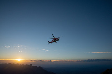 Fototapeta na wymiar Hubschrauber, der über Landschaft gegen den Himmel in den Sonnenuntergang fliegt