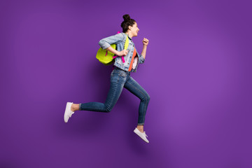 Fototapeta na wymiar Full length profile photo of pretty student lady jumping high rushing home after first studying day wear green bag casual denim outfit isolated purple color background