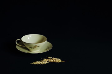 Exquisite tea cup on saucer made of thin porcelain with original floral ornament and ears of wheat on black background. Concept of beauty, retro, style, chic, luxury. Minimal style.