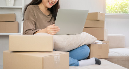 Young entrepreneur, sitting on the sofa and working at home. Checking orders from customers by laptop and writing customer address deliver shipment online sales. Concept of small business owner.