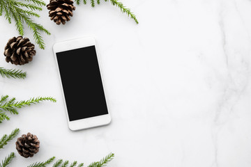 Smartphone with blank screen is on top of white marble table with Christmas decorations. Top view with copy space, flat lay.