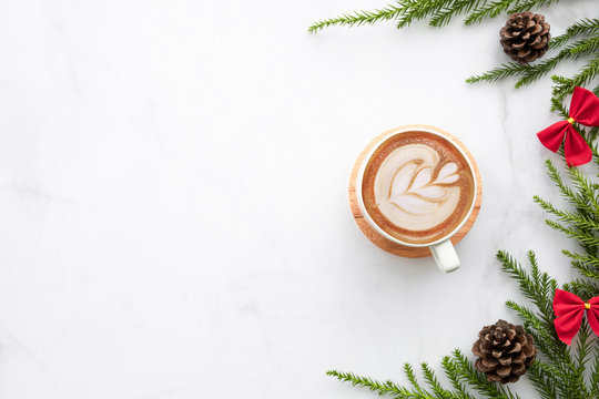 White marble table with cup of latte coffee and Christmas decoration with pine branches and pine cones. Christmas and new year celebration concept. Top view with copy space, flat lay.