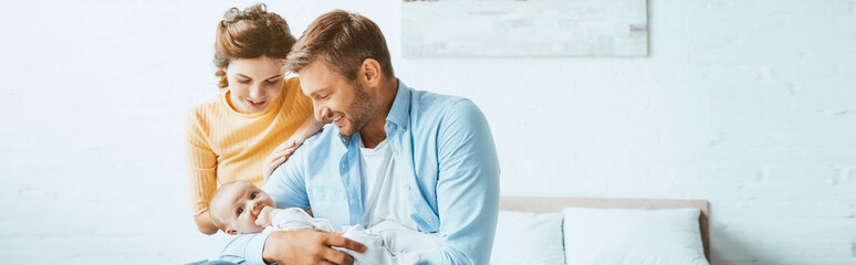 happy parents smiling while sitting on bed with little daughter