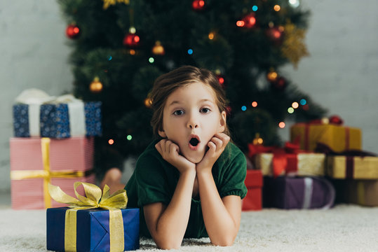 surprised child lying on floor near gift box and looking at camera