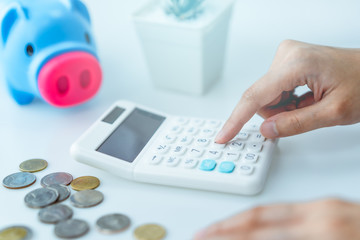 Financial Concept, hand using calculator with blue piggy bank and coins on white table background