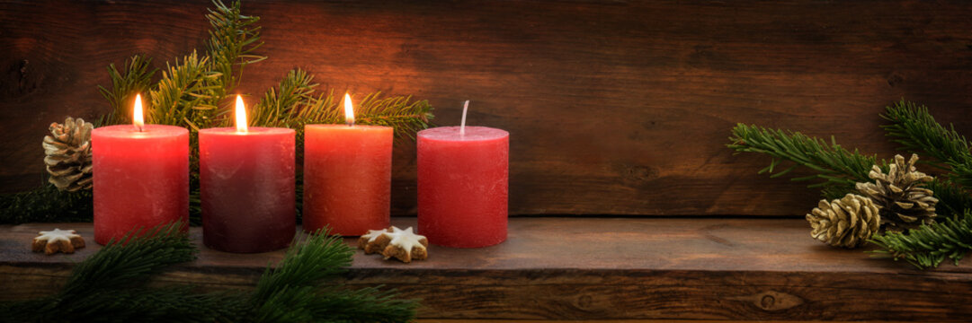 Third Advent, three of four red candles are lit with a flame, fir branches and Christmas decoration on dark rustic wood, wide panoramic format with copy space
