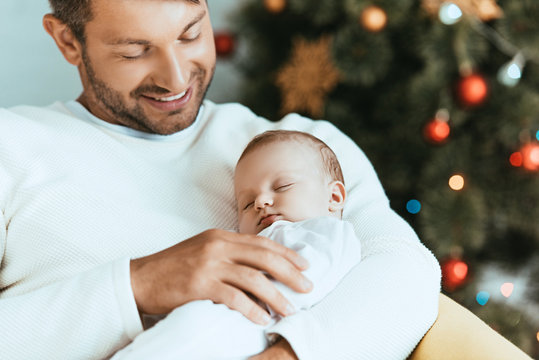 smiling father holding sleeping baby near christmas tree