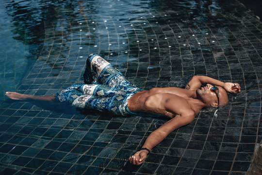 Attractive and relaxed Arabic shirtless male in turquoise sarong lying in the pool in a sunny day; vacation concept.