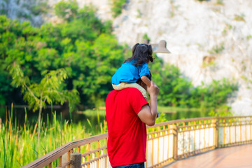 The Asian family is happy. Father and daughter are having fun and enjoying the journey. The child sits on the father's shoulder