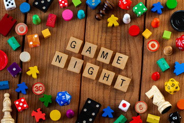 "Game Night" spelled out in wooden letter tiles. Surrounded by dice, cards, and other game pieces on a wooden background