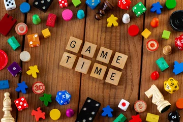 Fotobehang "Game Time" spelled out in wooden letter tiles. Surrounded by dice, cards, and other game pieces on a wooden background © Mitch