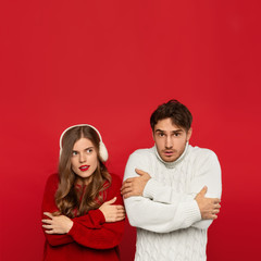 young couple in winter outfit feeling cold isolated on red background. Christmas concept