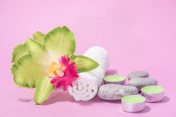 Fototapeta na wymiar White soft terry towels, orchid, stones and candles for skin care and spa on a pink background