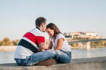 Couple in jeans sitting facing each other by the river