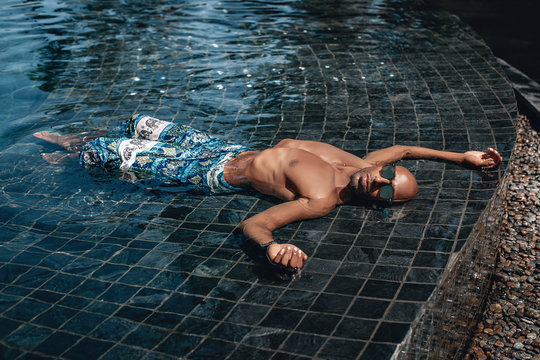 Attractive and relaxed Arabic shirtless male in turquoise sarong lying in the pool in a sunny day; vacation concept.