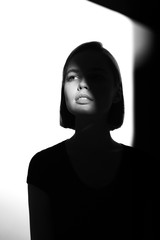 Fototapeta premium Fashionable beauty portrait. Black silhouette on white background. Girl with a spot of light on her face. 