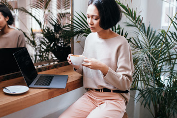 Young female asian adult drinking coffee and working on laptop
