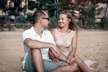 Obraz premium Luminous girl and her boyfriend are affectionately holding hands while sitting on a sandy beach in Thailand.