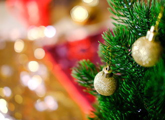 Christmas tree branch. Cozy . Two small cristmas-tree balls with golden glitter hang on needles of lush green. The background is blurred, red and golden, bokeh