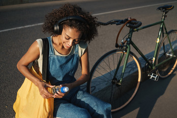 Positive young african woman listening music with headphones.