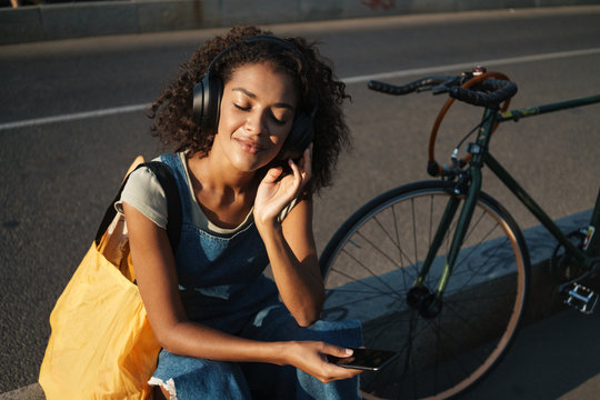 Cheery young african woman listening music with headphones. - Powered by Adobe