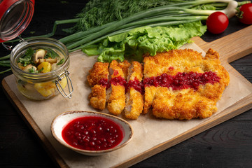 chicken schnitzel on a board with herbs and sauce in a cup