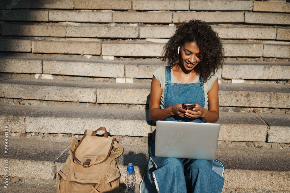 Poster woman sit on steps by street listening music.