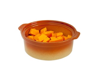 Ceramic tan pan filled with chopped pumpkin slices. Close up on a white background. Isolated