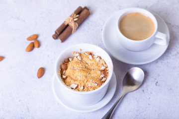 Crumble with apples, cinnamon and almonds in a white ramekin. In the background is a cup of coffee. Close-up, selective focus.