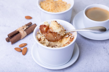Crumble with apples, cinnamon and almonds in a white ramekin. In the background is a cup of coffee. Close-up, selective focus.