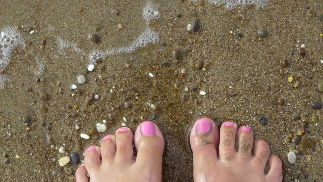 Top view of two barefoot pedicured female feet with beautiful pink gel polish pedicure at nails of toes. Happy woman standing on sandy tropical beach enjoying warm water. SLow motion video footage.