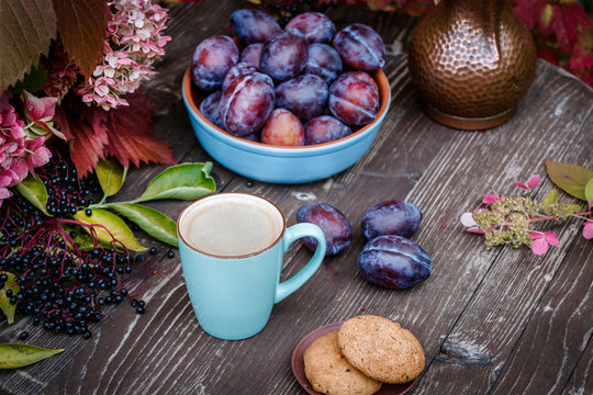 Fruits in a blue cup on a wooden table, plums, black elderberry, leaves of wild grapes, coffee, morning still life in the garden