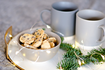 On a marble tray with a gold rim, there are two gray cups of tea and a chocolate gingerbread cookie. A treat for Santa Claus. Christmas tree branch with garlands decorate the new year card. Copy space