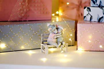 Many gifts wrapped in pink and gray paper, decorated with air ribbons with a bow, garlands are on the table from Santa Claus. New Year's miracle. Christmas greeting card with hugging mice. Copy space