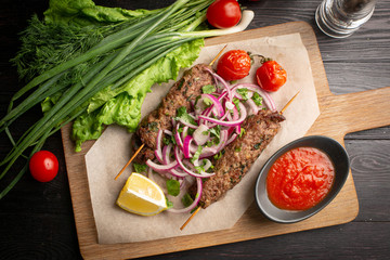 lula kebab of beef on skewers with onions, greens, ketchup and lemon on a board