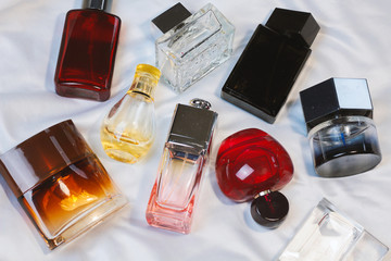 Colorful fashion trendy bottles of perfume toilet water fragrances  lie on a silver gray sheet on the bed, top view. Female and male fragrances 