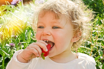 pretty little girl biting into a juicy strawberry