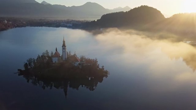 Aerial view of Bled Island (Blejski otok) with pilgrimage church of the Assumption of Mary and Bled castle on Lake Bled at clear autumn morning with light fog, Slovenia