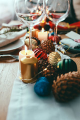 Table served for Christmas dinner in living room.  Close up view, table setting,plates, branch decoration, candles and gliterring toys on wooden table background. Winter decoration