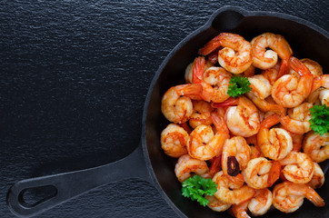 tasty roasted shrimps in a cast iron pan with parsley and garlic, on black background