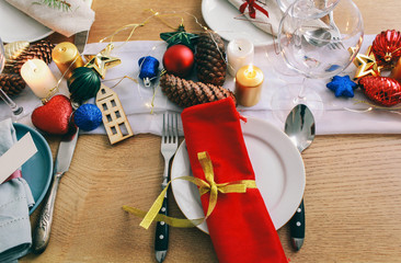 Table served for Christmas dinner in living room.  Close up view, table setting,plates, branch decoration, candles and gliterring toys on wooden table background. Winter decoration