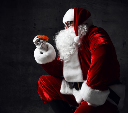 Santa Claus is holding red salmon caviar sandwich, looking at it going to eat. New year and Merry Christmas concept