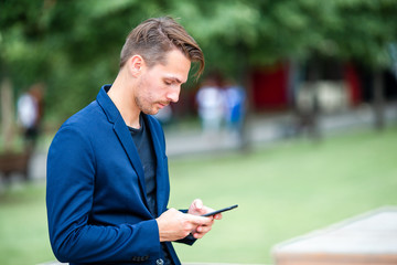 Fototapeta premium Man is reading text message on mobile phone while walking in the park