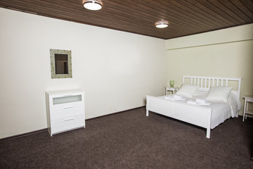 White room in the hotel with a double bed, pillows and a cabinet with mirror on the wall; accommodation concept.